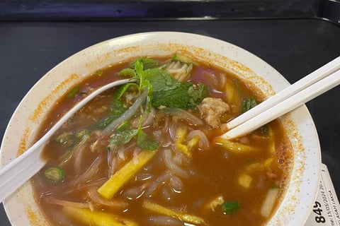 laksa, a noodle dish with a fish and tamarind based broth topped with anchovies cucumber and mint