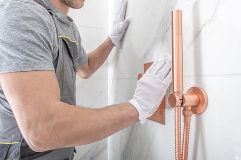 a hanndyman in a grey shirt and gloves is holding a shower head in Vancouver