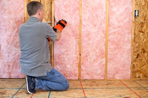 a man in a gray shirt and orange gloves installing insulation in Squamish