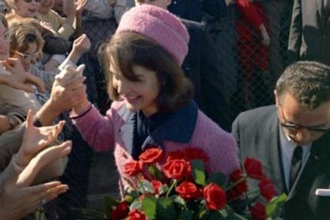 Jackie in a pink coat and hat is surrounded by a crowd of people