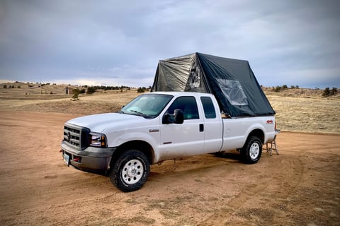 A truck with a fold-out overlanding tent on it's bed on a dirt road