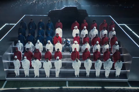 Kendrick Lamar performing in the middle of a group of people wearing red white and blue in the pattern of the American flag.
