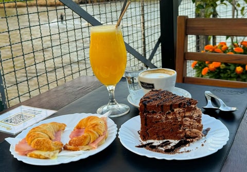Bolo de chocolate, Medialunas recheadas com presunto e queijo, café e suco de laranja sobre uma mesa