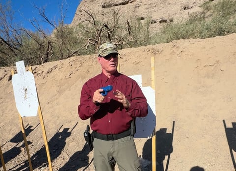 firearms instructor demonstrating shooting tactics with a blue training gun, work space