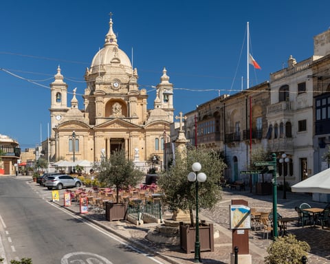 Nadur village square, with restaurant tables and parasols in the sunshine.