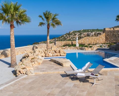 A swimming pool in a terrace with two palm trees, overlooking the sea.