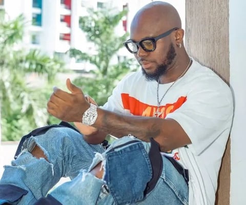 King Promise in a white shirt and blue jeans trousers.