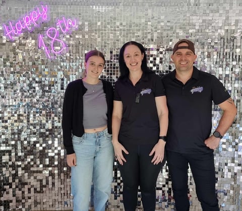 Laura with Carly and Kahn from Sweetaz Co. in front of a silver shimmer wall with a Happy 18th neon sign.