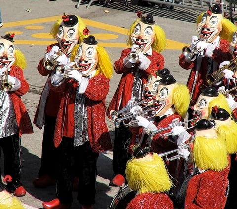 Figures dressed as clowns, playing trumpets. 