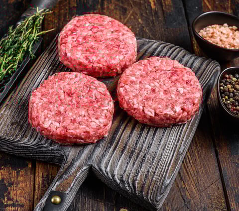 three uncooked hamburger patties on a cutting board