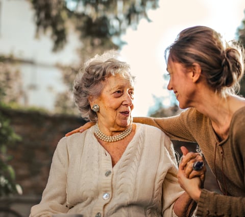 A young carer smiling and holding hands with an elderly woman