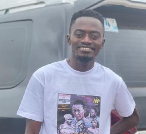 Lil Win in a white tee shirt standing infront of a car.