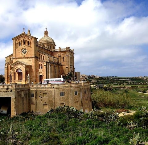 The Basillca of Ta Pinu, set in green fields and a cloudy blue sky.