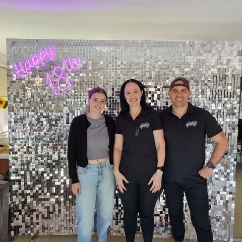 Laura and SweetAz crew in front of the silver shimmer wall and happy 18th neon after relocating.