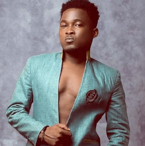 Bless posed in a green shirt with an Adinkra symbol.