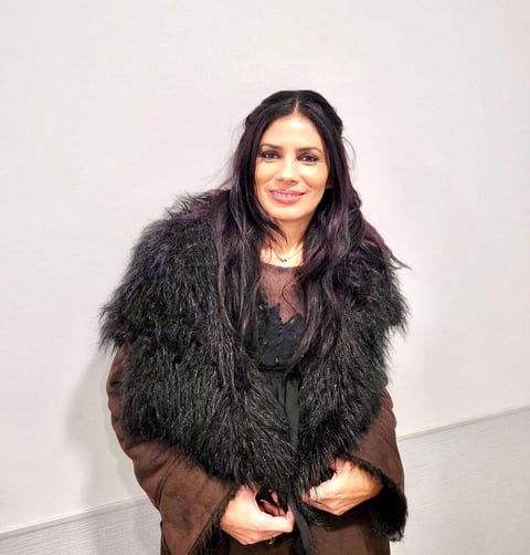 Raquel Alves posing for the camera with a brown furred coat and a smile.