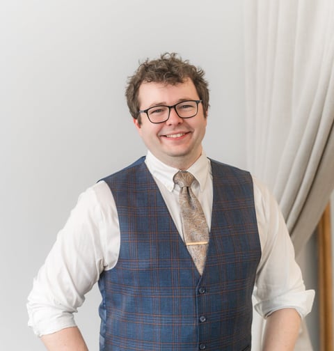 Picture of Rocco Catrone smiling at camera with glasses, a gold tie, and vest.