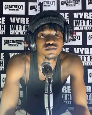 Kwesi Amewuga in a black sleeveless shirt behind a microphone.
