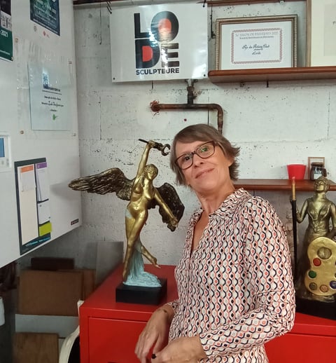 Photo de l'artiste sculpteure Lode dans son atelier posant à côté de ses sculptures