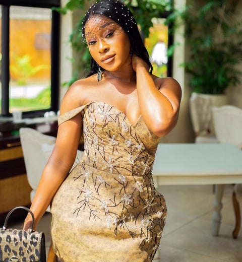 Efia Odo in a stunning brown striped dress with a leopard skinned bag.