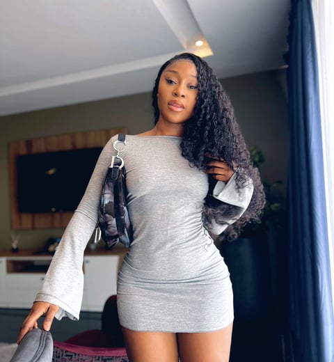 Efia Odo in a gray overall dress with a black handbag.