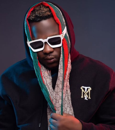 Medikal in a wine sweater wearing dark sunglasses.