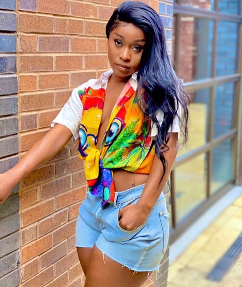 Efia Odo in a designed shirt and jeans shorts standing close to a wall.