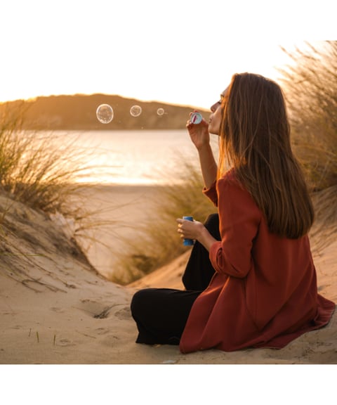 a woman blowing bubbles in the sand