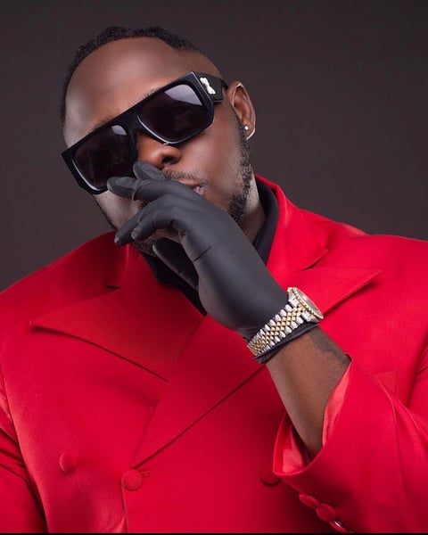 Medikal in a red shirt wearing dark sunglasses.