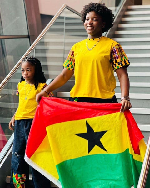Afronita and Abigail in matching African prints holding a Ghana flag.