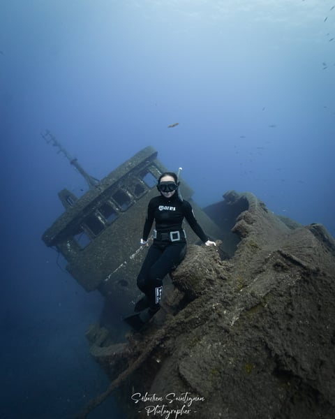 a freediver posing over a wreck ship. Photo taken by Sébastien Saintignan