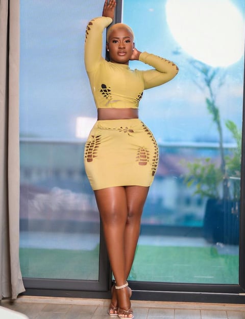 Fella Makafui in a yellow designed top and down posed by a glass window.