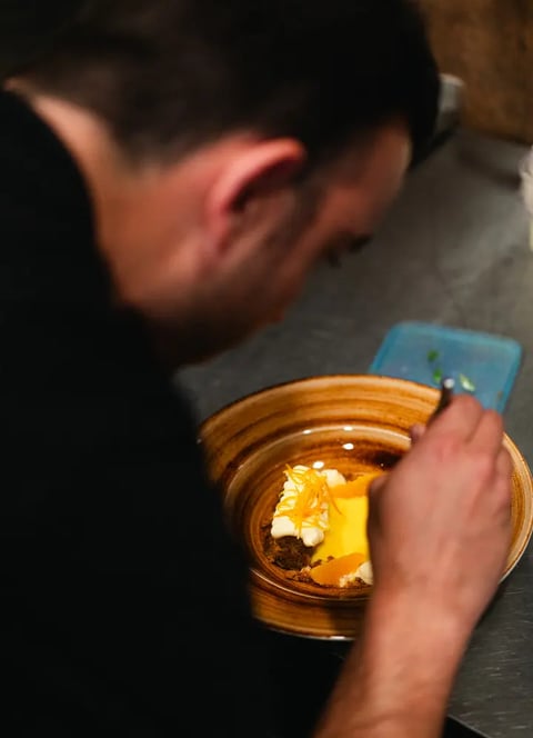 Nico, chef de Es Mestral, finalizando la presentación de un postre de naranja con crema y ralladura cítrica en la cocina del