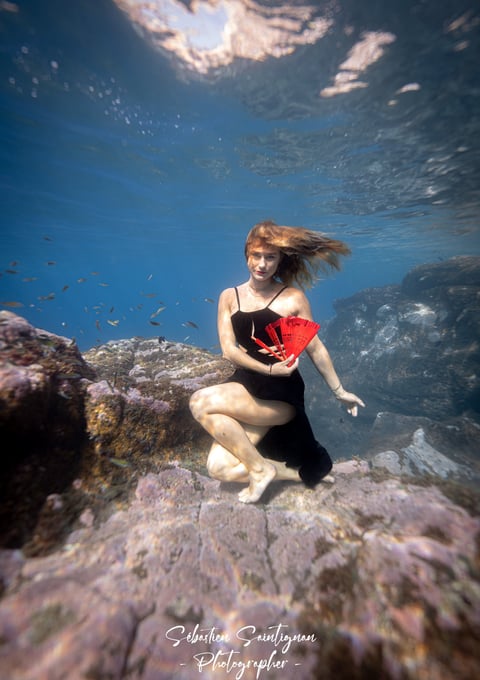 Underwater model posing on a rock with a fan. Photo by taken Sébastien Saintignan.