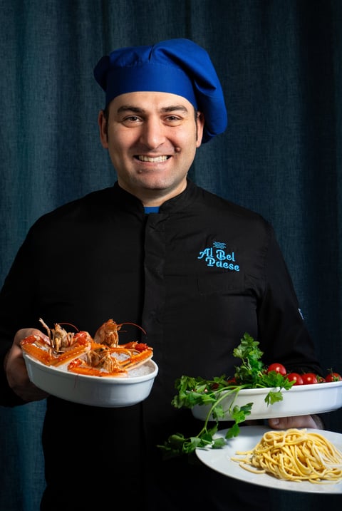 Chef Vito Amodio che presenta ingredienti freschi per la cucina: scampi, pasta fresca e pomodori