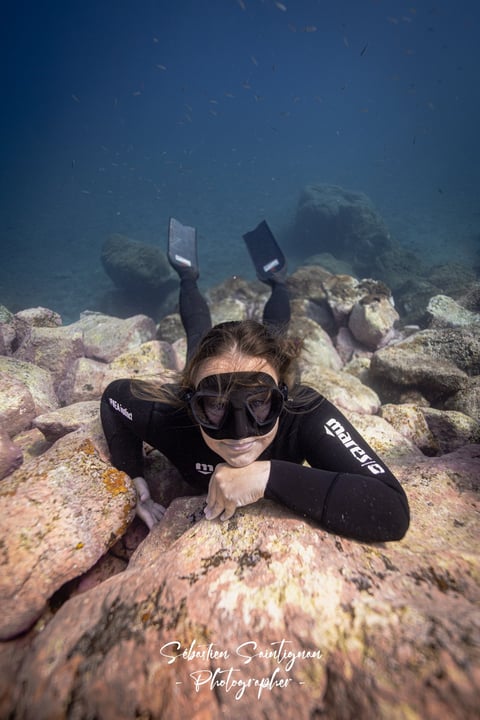 A freediver in a wetsuit is posing for an underwater photoshoot. Photo taken by Sébastien Saintignan