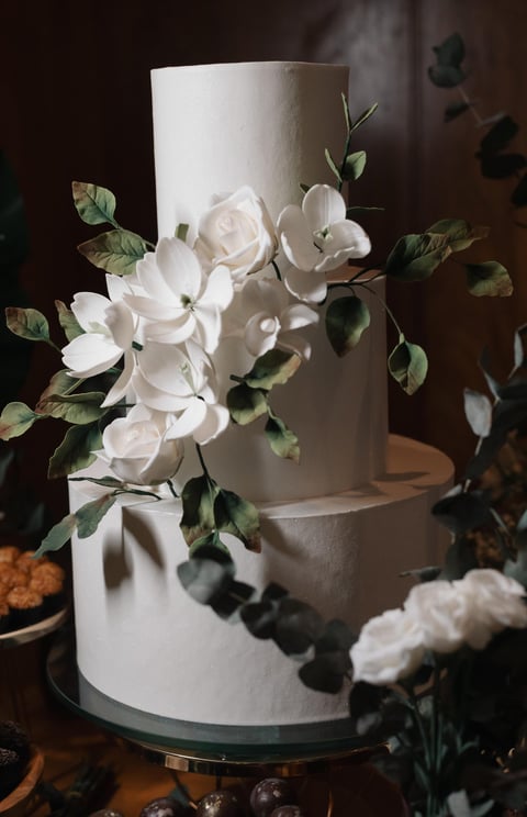 Imagem de um elegante bolo de casamento branco com flores e folhagens decorativas, perfeito para fes