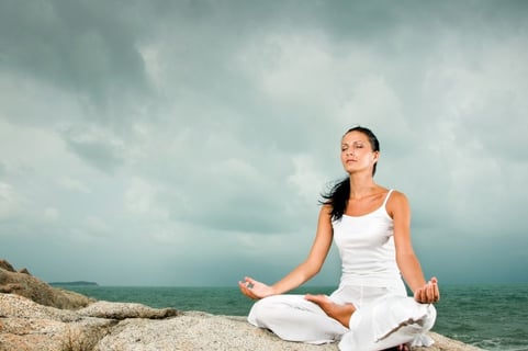 woman meditating on a rock by the ocean