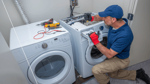 a man in a blue shirt and red gloves is fixing a washing machine