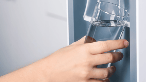 a person holding a glass of water in front of a refrigerator