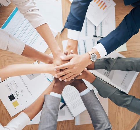 group of business people stacking hands over a table covered with charts and graphs