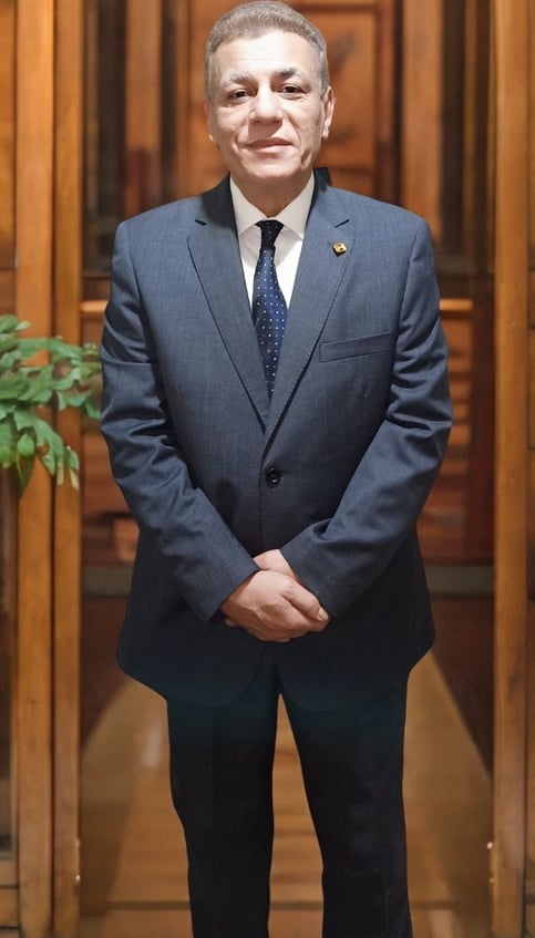 Major General Ayman Syedelahl stands wearing an elegant grey suit, with luxurious office decor 