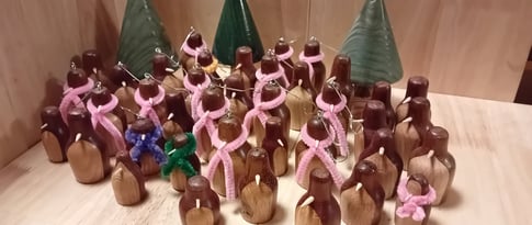 A group of turned wooden penguins in dark wood with light front and light beak. Some wearing pipecleaner scarfs