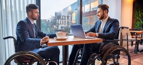 Zwei Rollstuhlfahrer sitzen für ein Beratungsgespräch in einem Café