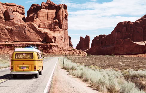 a yellow van driving down a road with moutain rocks in the background