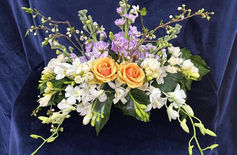 Aranjament cu trandafiri galbeni, flori albe și mov pe fundal albastru.