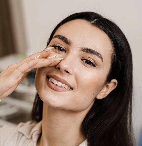 Smiling woman gently touches her nose, showing satisfaction.