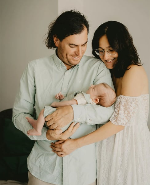 Parents souriants à la maison, regardant leur bébé dans les bras du papa – séance naissance domicile