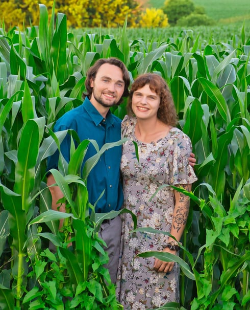 a man and woman standing in a corn field