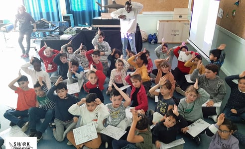 Une classe primaire qui fait le signe de reconnaissance du requin